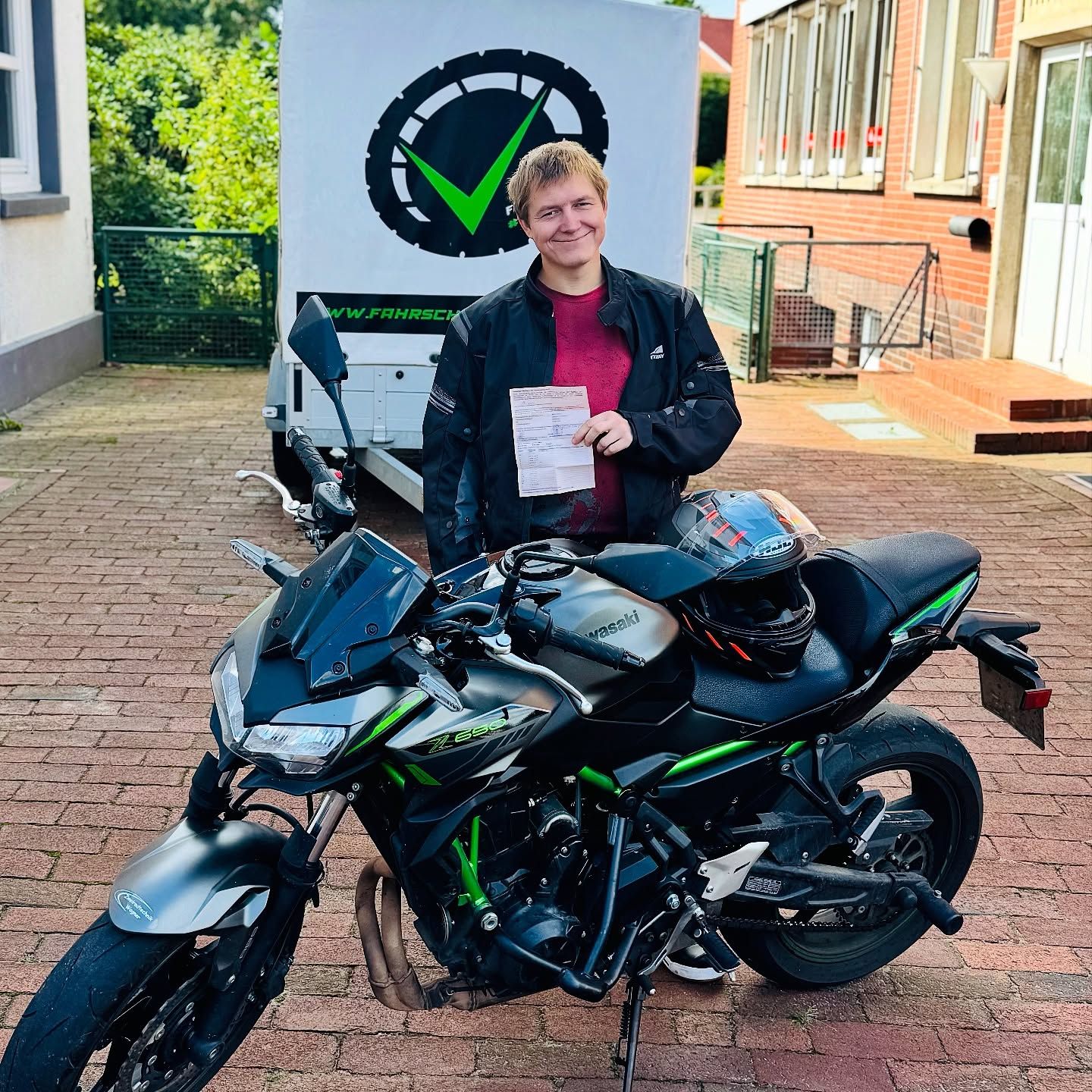 Ein Fahrschüler mit Prüfungsbescheinigung neben dem Motorrad der Fahrschule